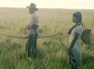 베네수엘라 야노스 지역에서 사냥과 채집 여행을 하는 사바나 푸메족(Yaruro people) 부부. 남자는 활, 강철촉이 달린 화살 세 개, 그리고 사슴에 접근하기 위한 위장용으로 재비루황새 머리를 닮은 모자를 들고 있다. 여자는 강철촉이 달린 땅파는 막대기와 야생 덩이줄기를 채집하기 위한 바구니를 들고 있다.