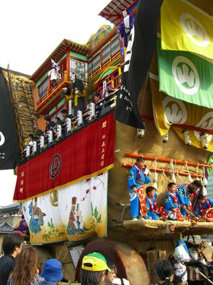 나나오의 세이하쿠사이 축제에서 군중 사이로 지나가는 바퀴 달린 큰 미코시, 데카야마