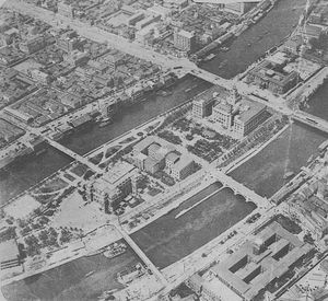 나카노시마와 공원, 중앙 삼각주의 왼쪽 부분이 보인다. 삼각주의 맨 왼쪽에 있는 첫 번째 건물은 오사카 시립 중앙 공회당이며, 오른쪽으로 오사카 부립 나카노시마 도서관, 오사카 시청, 일본 은행 오사카 지점이 차례로 이어진다. 은행 앞 거리는 미도스지의 일부이다. - 1930.