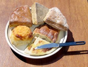 시계 방향으로 아래부터: 버터를 바른 따뜻한 감자 스콘과 치즈 스콘, 윤기 나는 납작한 트리클 스콘, 그리고 과일 스콘 위에 밀크 스콘