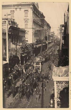 위에서 본 도시 거리 풍경, 왼쪽 아래에서 오른쪽 위로 비스듬히 보이는 거리, 많은 사람들이 거리를 따라 줄지어 서 있고, 말, 마차, 사람들이 행진하고 있음