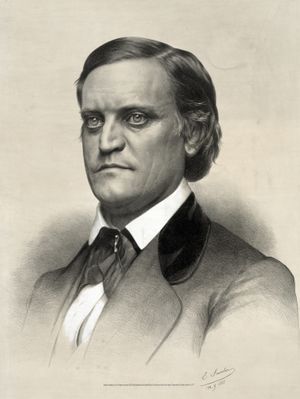 짙은 머리카락과 크고 둥근 눈을 가진 남성이 깃이 높은 흰색 셔츠, 검은색 재킷, 검은색 넥타이를 착용하고 있는 모습