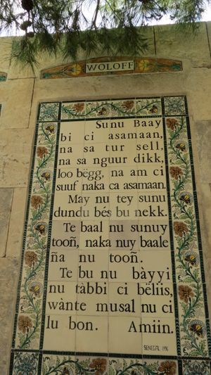 예루살렘에 있는 주기도문이 라틴 문자로 쓰인 볼로프어로 적혀 있습니다. 'ë', 'é', 'à', 'ñ'과 같은 문자가 보이고, 겹자음과 긴 이중 모음도 보입니다.