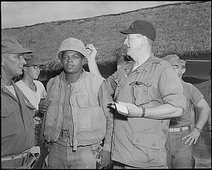 1966년 6월, 베트남 남부 주라이 방문 중 병장 폰젤 워포드의 헬멧에 서명하는 웨인