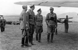 잔디밭 비행장의 항공기 날개 아래 서 있는 이탈리아 장교 세 명과 독일 장교 세 명