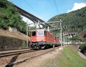 복합 운송 열차가 RE 4 4에 의해 이끌리고, RE 6 6가 비아스치나 루프를 통과한 직후 따라온다. 3개의 트랙 레벨은 관련 전철화 갠트리를 통해 식별할 수 있다. 다양한 콘크리트 구조물은 도로를 지탱한다.