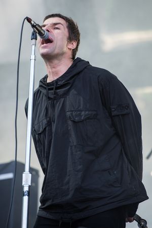 리암 갤러거의 노래 자세: 팔을 뒤로 하고 머리를 마이크 쪽으로 젖힌 모습