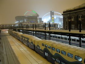 밝게 빛나는 경기장 근처 기차역의 마지막 통근열차. 경기장 지붕 받침대는 크리스마스 시즌을 맞아 녹색과 빨간색 조명으로 장식되어 있습니다.