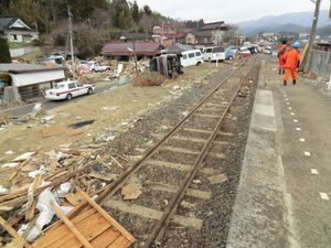 동일본 대지진으로부터 1개월 후의 시시오리카라쿠와역. 승강장 주변은 쓰나미로 떠내려간 잔해가 흩어져 자동차들이 선로를 막고 있다.