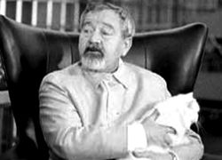 짧고 희끗희끗한 머리, 콧수염과 턱수염을 기른 중년 남성이 고양이를 안고 있는 상반신 사진.