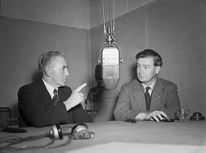 Iorwerth Thomas와 Gwynfor Evans가 BBC 마이크 앞 테이블에 앉아 토론하고 있다.