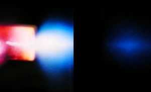 석영 모세관이 있는 캐필라리트론(Capillaritron)이 진공 챔버 내에서 작동 중: 왼쪽에는 플라즈마가 추출 음극까지 이르는 빛나는 모세관이 있고, 오른쪽 뒤에는 푸르스름하게 빛나는 이온 빔이 있다.