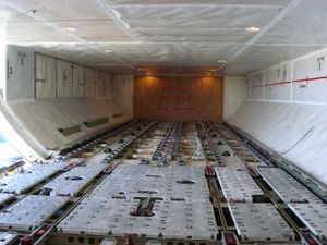 보잉 747 전면 하부 수하물칸. 바닥의 ULD용 롤러와 "주의: 충격 금지 – 내부에 식수 탱크 있음"이라고 표시된 칸막이에 유의