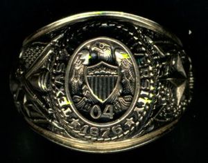 금반지의 근접 촬영. 윗면에는 텍사스 A&M 대학교 1876이라는 글자가 독수리가 방패 위에 있는 0과 4라는 숫자를 둘러싸고 있다. 왼쪽에는 큰 별과 참나무가 있다. 오른쪽에는 대포, 사브르, 소총과 미국과 텍사스의 십자기가 있다.