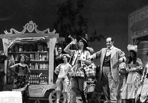 1968년 신시내티 오페라의 "와일드 웨스트" 버전 사랑의 묘약 공연에서 떠돌이 돌팔이 의사이자 "묘약"과 기타 강장제를 파는 사람인 "둘카마라 박사" (Andrew Foldi)가 그의 교활한 트럼펫 연주 조수 "코치스" (Bruce Cooper)에게 제1막(2장) 아리아 "Udite, udite, o rustici" (들어라, 들어라, 농부들이여)를 부르기 위해 마을 사람들을 불러 모으라고 손짓하는 모습. 1832년 오페라의 배경은 바스크 지방의 마을에서 1870년대 텍사스로 옮겨졌다.