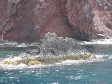 서쪽 해안의 상세 사진은 붉은색 화산암 절벽과 조간대 조류 지역이 보이는 작은 바위섬을 보여준다. (2011년 촬영)