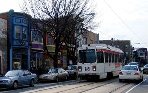 도로를 달리는 흰색 단일 차량 트롤리. 도로변 주차와 2차선 도로의 이중 트랙이 결합되어 자동차 기동성이 제한됨