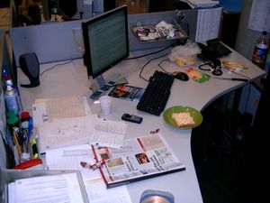 칸막이 책상. 컴퓨터 부품과 종이 문서가 공유하는 공간을 보여줌