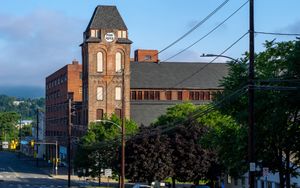 카메라 앞 거리 오른쪽에 뾰족한 지붕이 있는 벽돌 타워. 배경에는 푸른 언덕이 있다.