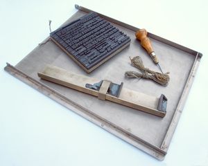 손으로 조판하는 데 사용되는 도구: 묶인 활자 조각, 조판 틀, 활자 송곳, 그리고 끈이 활자 통에 놓여 있음