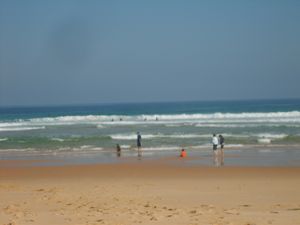 넓은 모래 해변과 파도가 치는 바다, 멀리 보이는 곶