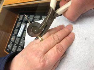 반지 절단기로 끼인 반지를 제거하는 보석 세공사. 절단기에는 반지 아래에 가드가 있고, 원형 톱날을 손으로 돌려 반지를 자른다.