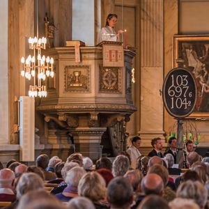 강단에 서서 예복을 입고 있는 사람은 성직자이고, 아래에 앉아 있는 사람들은 평신도이다.