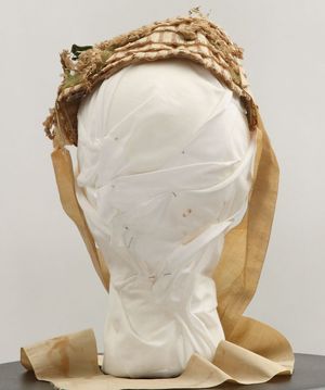 여러 겹의 짚, 베이지색 꽃 스프레이, 녹색 잎, 베이지색 실크 리본 끈이 달린 여성용 보닛.