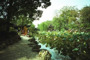 The Shizilin Garden in Suzhou. Men and women stand on curving rock formations overlooking a pond containing flowery plants.