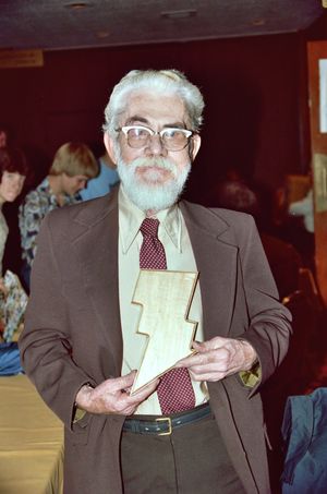 Beck는 정장을 입고 캡틴 마블의 슈트처럼 양식화된 번개 모양을 들고 있다