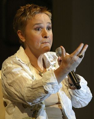 에더리지가 흰색 재킷과 민소매 셔츠를 입고 서서 라이브로 말하고 있다