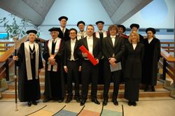 델프트 공과대학교의 박사 학위 논문 심사 후 전형적인 사진. 프로모벤두스(가운데)는 두 명의 파라님프와 함께한다. 페델은 왼쪽에 있으며, 지팡이를 들고 있다. 빨간 튜브는 박사 학위 증서를 담고 있다. 프로모벤두스뿐만 아니라 파라님프도 흰색 넥타이를 착용해야 하며, 심사 위원회의 모든 교수는 토가를 착용한다.