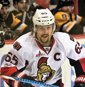 흰색 아이스하키 유니폼을 입고 수염과 콧수염을 기른 남자