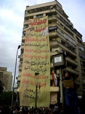 높은 아파트 건물에 걸린 대형 배너, 여성이 전경에서 표지판을 들고 있음