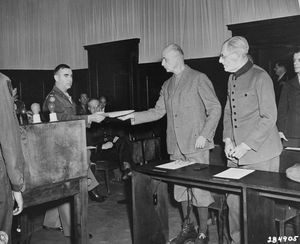 빌헬름 리스트가 인질 재판에서 기소장을 받고 있다. 그의 옆에는 막시밀리안 폰 바이흐스가 서 있다.