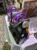 자주색과 검은색 탁상용 전동 물레 (e-스피너). 베이스의 전기 모터가 플라이어를 구동한다.