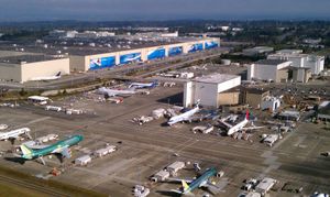 장비와 지상 차량으로 둘러싸인 여러 제트기가 있는 대형 공장과 공항의 항공 사진.