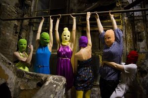 스키 마스크와 여러 가지 색상의 옷을 입은 6명의 여성 그룹이 작고 지저분한 벽돌 공간에 있다. 그들 중 4명은 팔로 바에 매달려 있고, 한 명은 근육을 자랑하며, 다른 한 명은 매달린 여성 중 한 명의 허리를 잡고 있다.