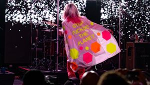 Harry viewed onstage from the back, wearing a pink coat that reads "STOP FUCKING THE PLANET" in yellow