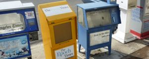 Empty newspaper vending boxes on the street, left to right, the Los Angeles Times (cut off), Epoch Times, a San Diego paper (Gone to the Web, sddt.com), a white unnamed box, and the San Diego Business Journal (cut off)