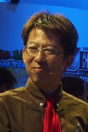 Kensuke Tanabe, a Japanese man wearing glasses, a brown shirt, and red tie