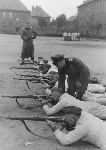 군용 약모와 작업복을 착용하고 육군 하사관에게 사격 동작 훈련을 받는 국민돌격대원. 손에 든 소총에는 Kar98k, Gew98, 체코슬로바키아제 Kar98k 단축형이 혼재되어 있다