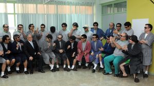 Color image of President Piñera visiting the rescued miners, who are dressed in hospital robes and pajamas while seated and standing in a semi-circle in a hospital room