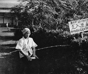 가시 철조망 뒤에 자신의 땅에 앉아 있는 노파, "출입 금지"라고 적힌 표지판, 1955년 9월