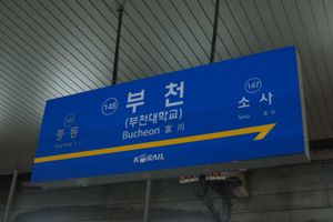 부천의 기차역 이름이 적힌 표지판. 상단에는 한글 표기가 있고, 그 아래에는 수정 로마자 표기법에 따른 라틴 문자 표기가 있으며, 한자 텍스트가 함께 있다.