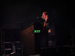 Martin performing with his microphone and piano, wearing a black outfit