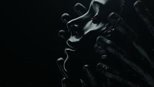 A woman, animated in a tar-like substance, is caressed by the hands of a man.