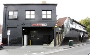 A black two-story building on a sidewalk