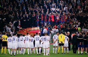 흰색 셔츠를 입은 남자들이 배경의 연단에 서 있는 파란색과 빨간색 셔츠를 입은 남자들을 바라보고 있다.