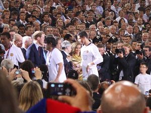 흰색 셔츠를 입은 남자가 정장을 입은 남자로부터 메달을 받고 있다.